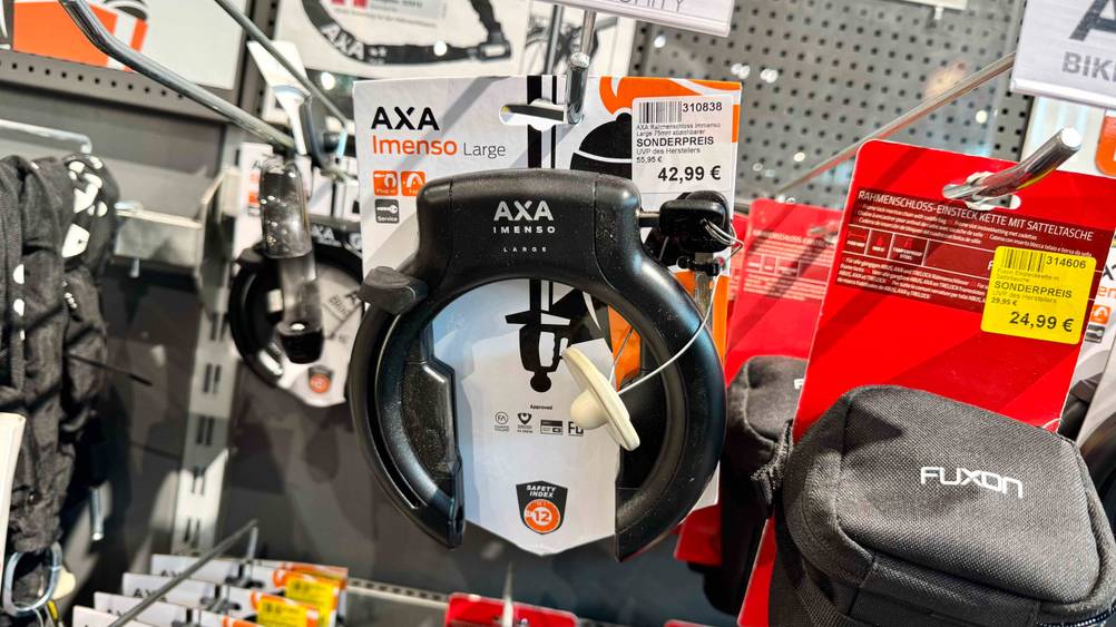 Ein getestetes Axa-Rahmenschloss hängt in einem Verkaufsregal neben anderen Produkten.