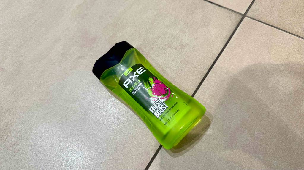 Eine Flasche AXE-Duschgel liegt getestet auf Fliesen.
