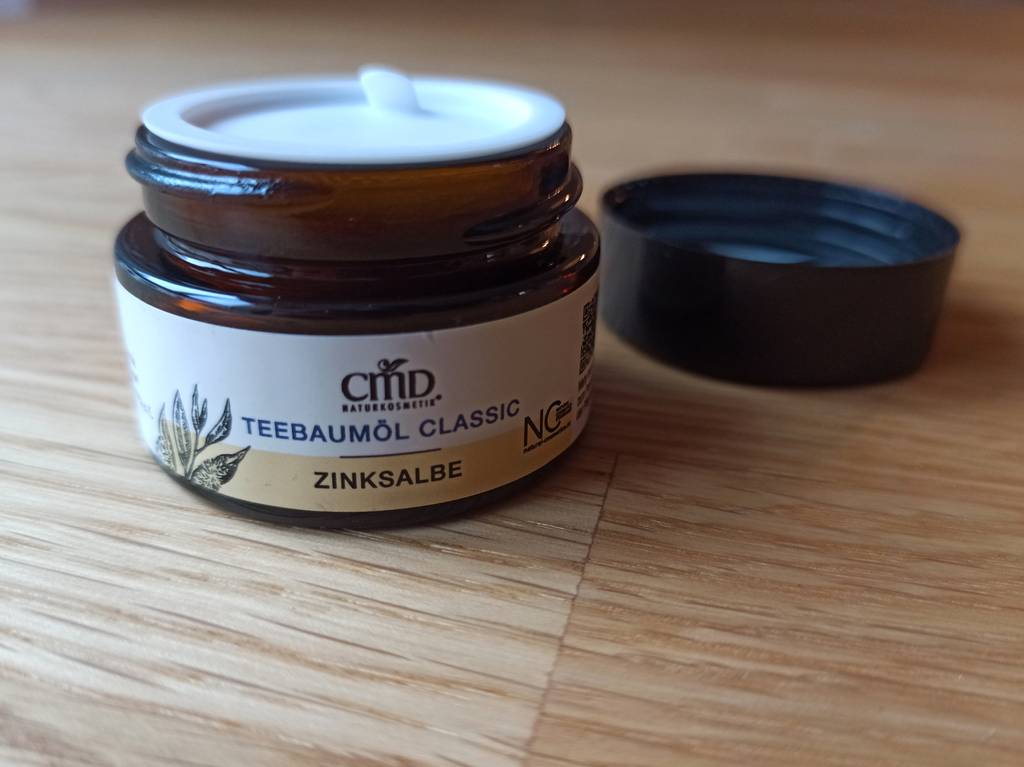 Ein dunkler Tiegel Anti-Pickel-Creme von der Seite.
