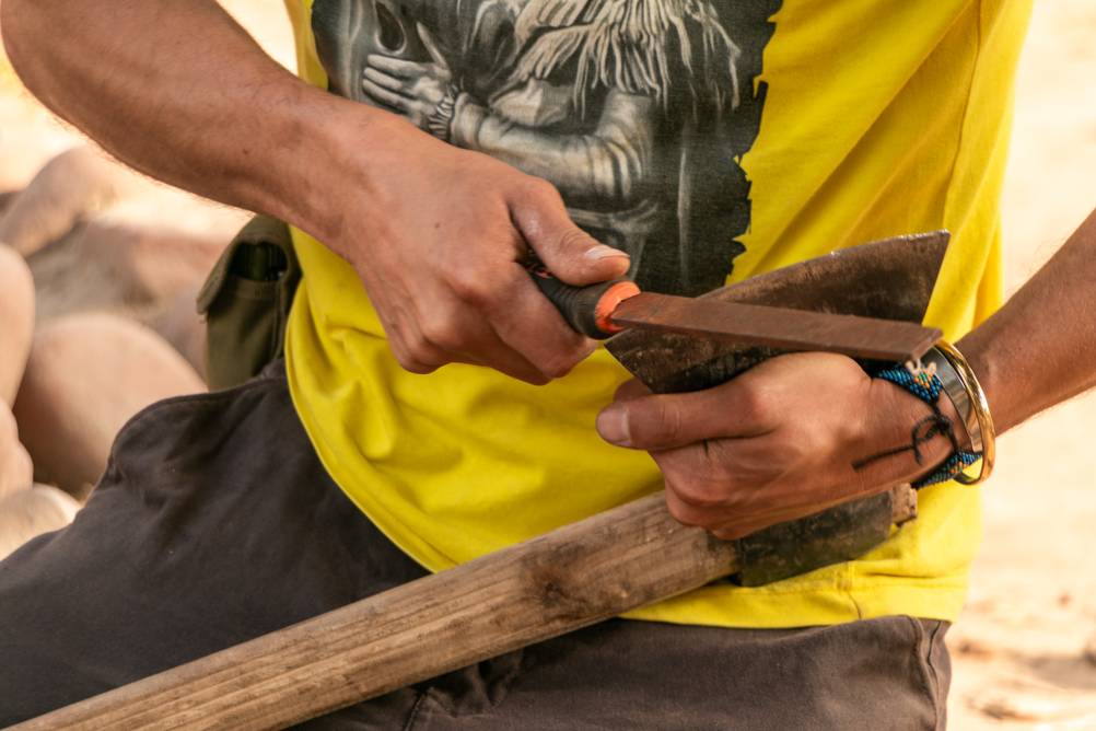 Axtschärfer im Test: Ein Mann in gelbem T-Shirt hält in der einen Hand eine Axt und setzt mit der anderen eine Feile an.
