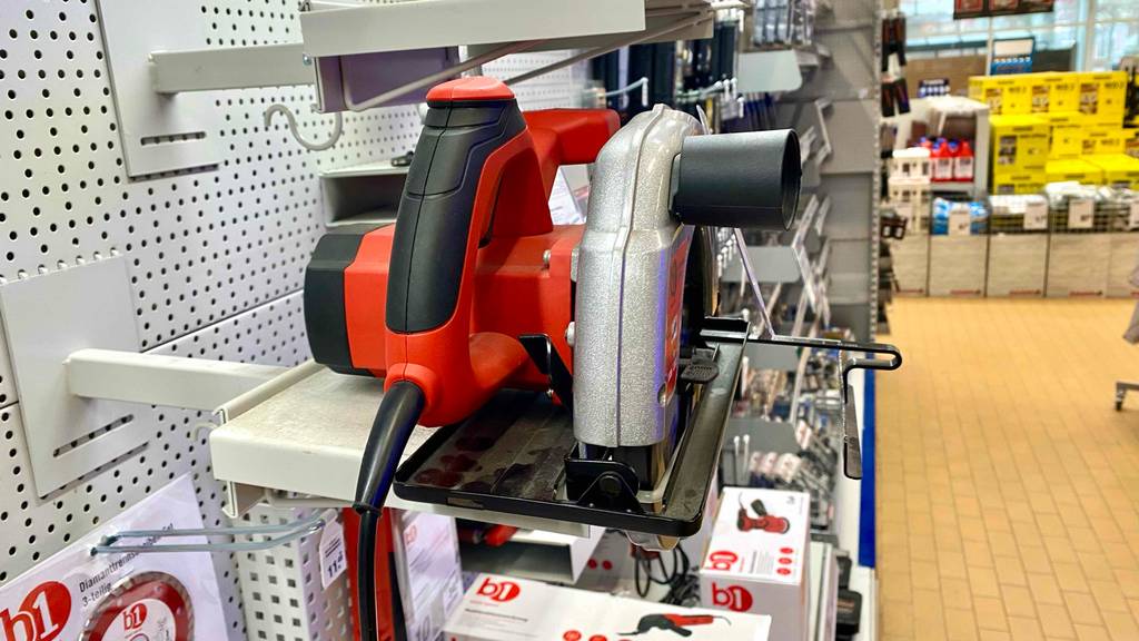 Handkreissäge im Test: ein b1 Modell in rot-schwarzem Design, inklusive Parallelanschlag, Führungslinie und Staubsaugeradapter auf einer Ausstellungsfläche inmitten von b1 Produkten im Baumarkt.