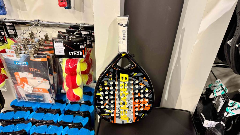 Ein Padel-Schläger lehnt zum testen an einer Wand, nebendran hängen Softbälle.
