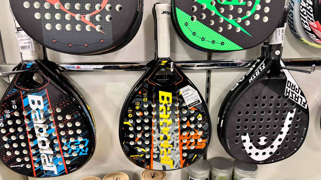 Padel-Schläger im Test: Mehrere unterschiedliche Variationen hängen an einem Wandregal.
