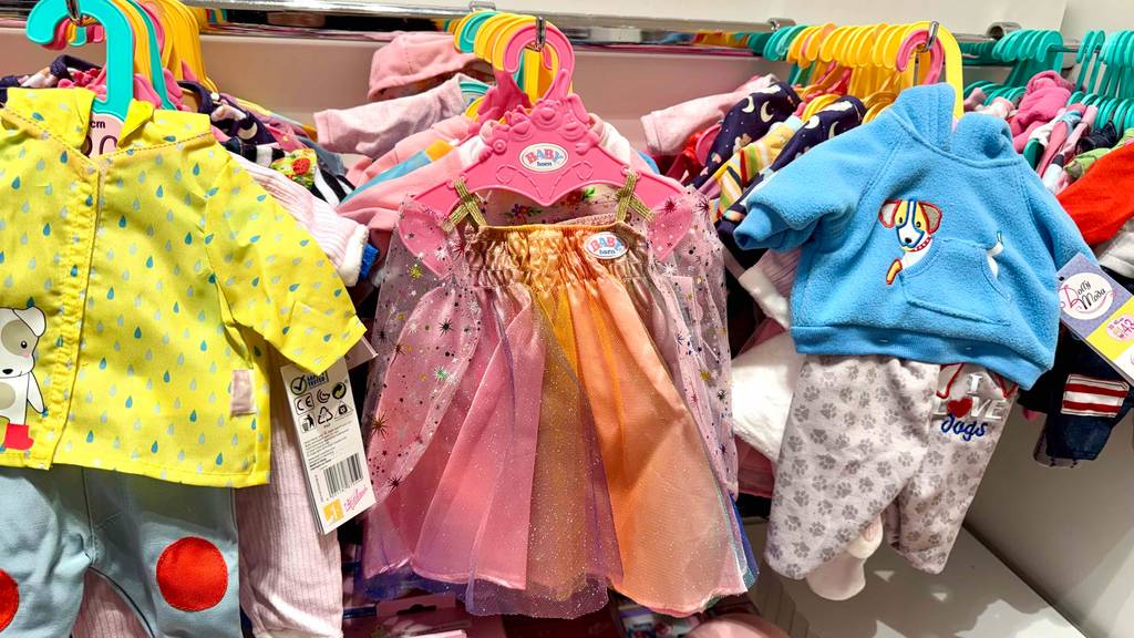 Puppenkleidung im Test: Viele verschiedene Ausführungen hängen hinter- und nebeneinander in einem Regal.