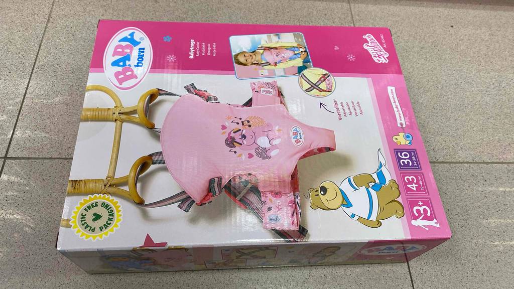 Im Test: Eine Verpackung mit einer Baby Born Puppentrage-Abbildung in Rosa liegt auf einem grauen Fliesenboden.