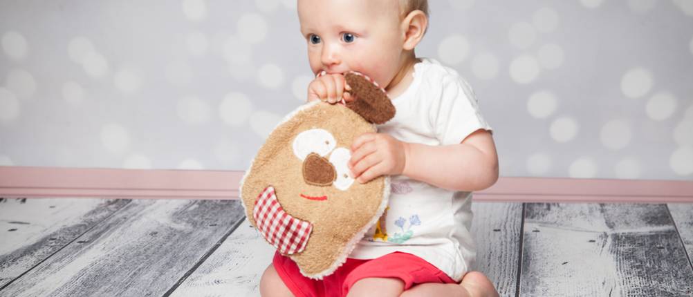 Baby-Kirschkernkissen-Test: Baby sitzt auf dem Boden und hält ein Kirschkernkissen