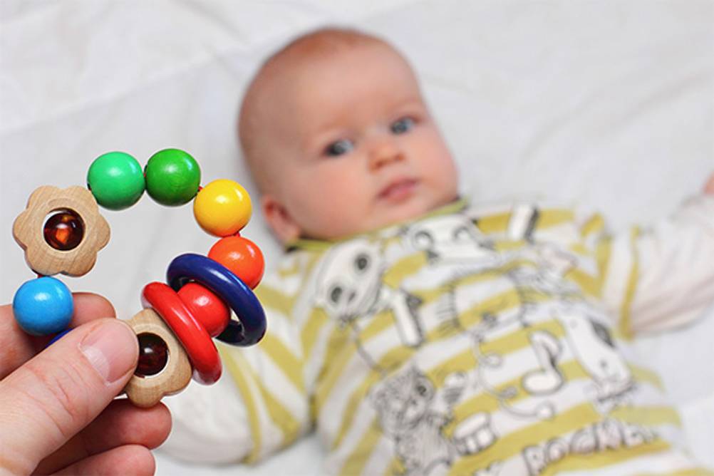 Baby-Spielzeug im Test: Hier ein bunter Greifling aus Holz. Das Baby blick gespannt darauf.