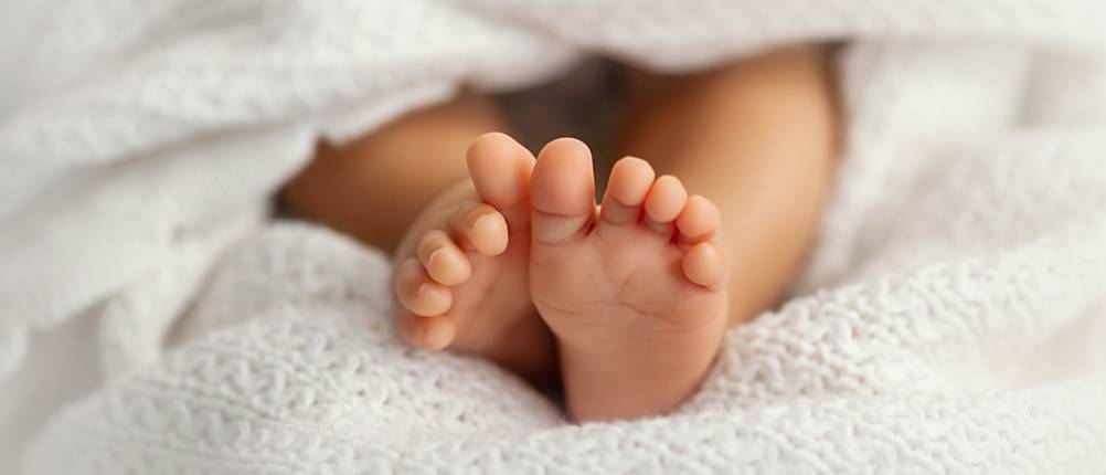 Babydecke im Test: Babyfüße unter weißer Babydecke.