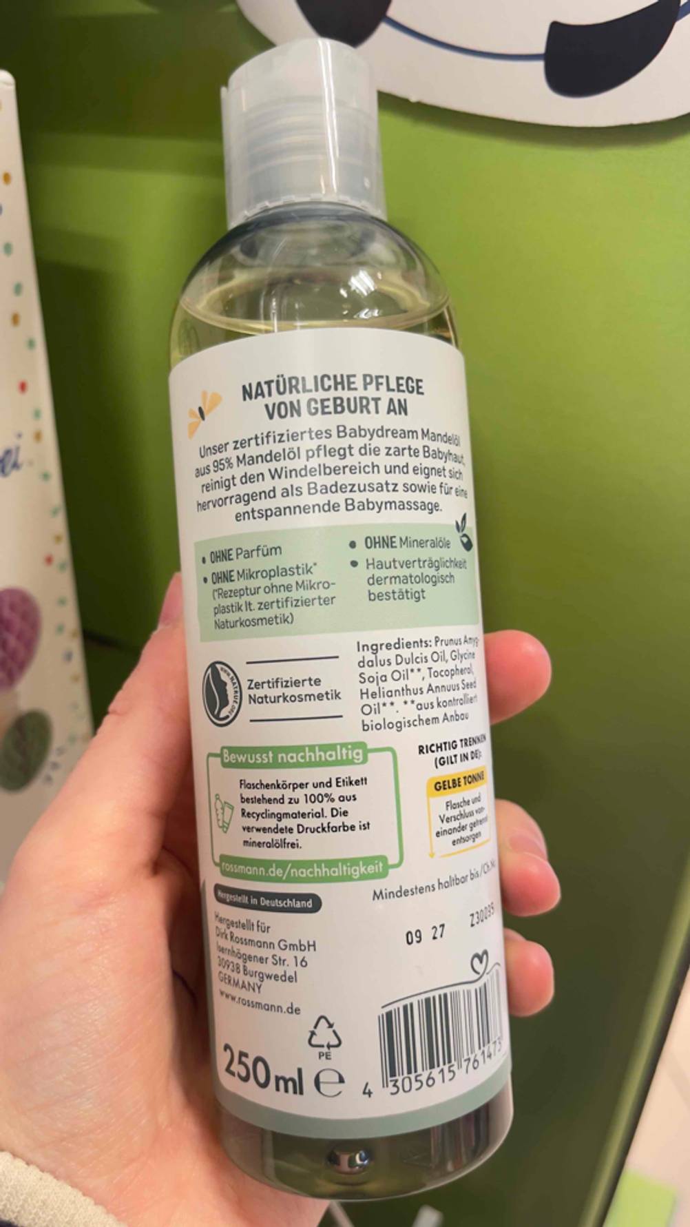 Eine Hand hält eine Flasche getestetes Mandelöl für das Baby mit der Rückseite nach vorn.