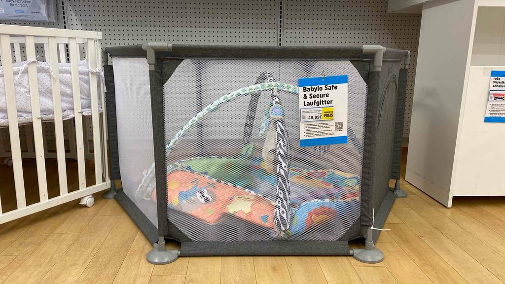 Getestet: Laufgitter steht aufgebaut mit Netz-Umrandung inklusive Reißverschluss-Öffnung zwischen weiteren Kindermöbeln in einem Verkaufsbereich.
