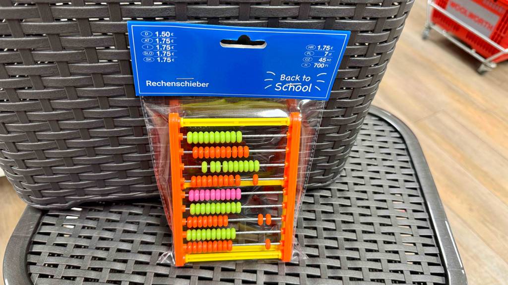 Ein Rechenschieber in transparenter Verpackung lehnt zum testen an eine geflochtene Box.