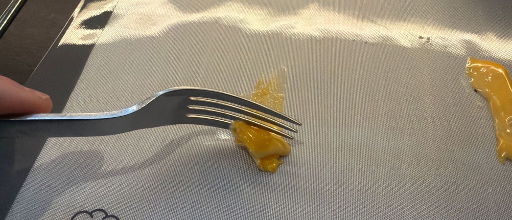 Mit einer Gabel werden Käsereste von der Backefix-Original-Backfolie gekratzt