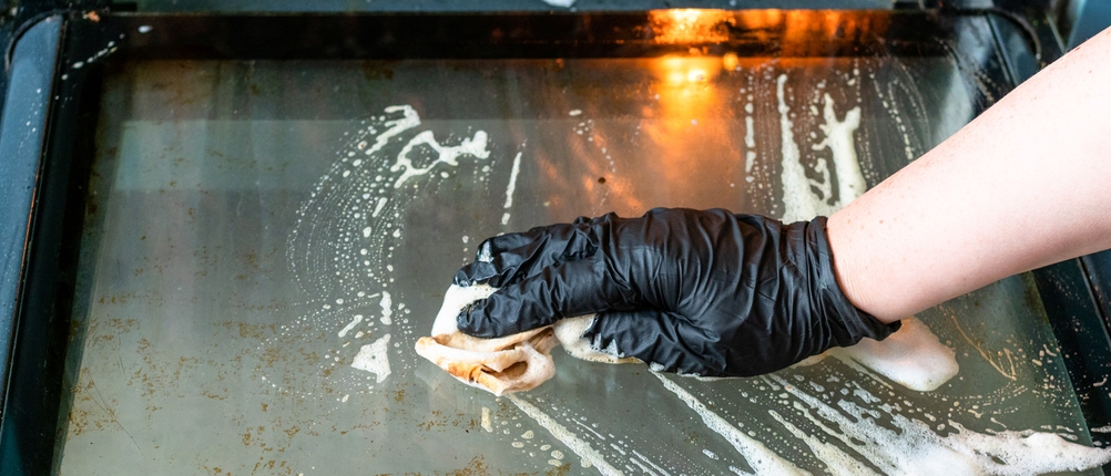 Eine behandschuhte Hand reinigt eine verschmutzte Ofentür.