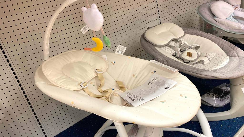 Babyschaukel-Test: ein Modell mit weißem Ständer und hellem Bezug steht in einer Reihe mit anderen Babyschaukeln im Verkauf.