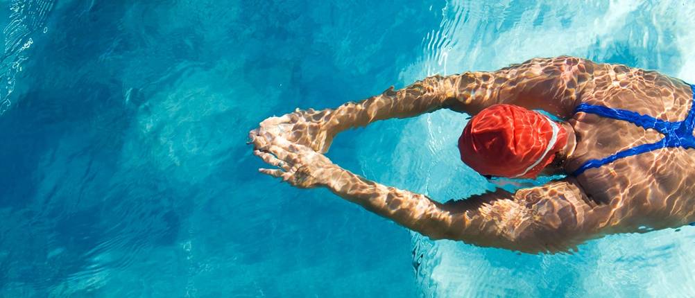 Frau mit Badekappe und Badeanzug taucht mit ausgestreckten Armen.