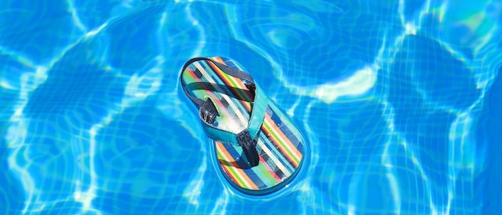 Badeschuhe für Kinder im Test: Ein bunt gestreifter Flip Flop schwimmt im Pool.