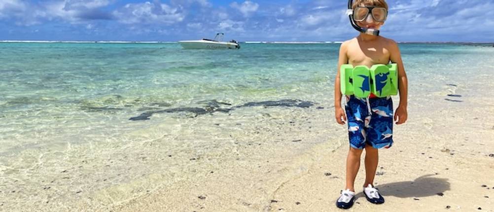 Badeschuhe für Kinder getestet: Ein Junge steht am Strand und ist mit einem Schwimmgurt und einer Schnorchelmaske sowie Badeschuhen ausgestattet.