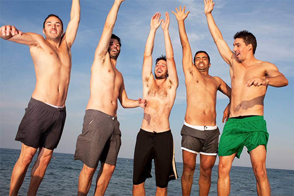 Badeshorts für Herren im Test: Fünf jubelnde Männer am Strand in Badehosen.