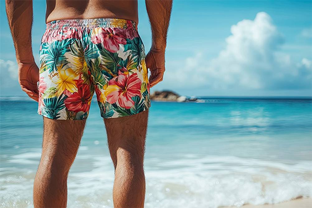 Badeshorts für Herren im Test: Ein Mann am Strand der eine Badeshorts mit tropischen Blumen trägt.