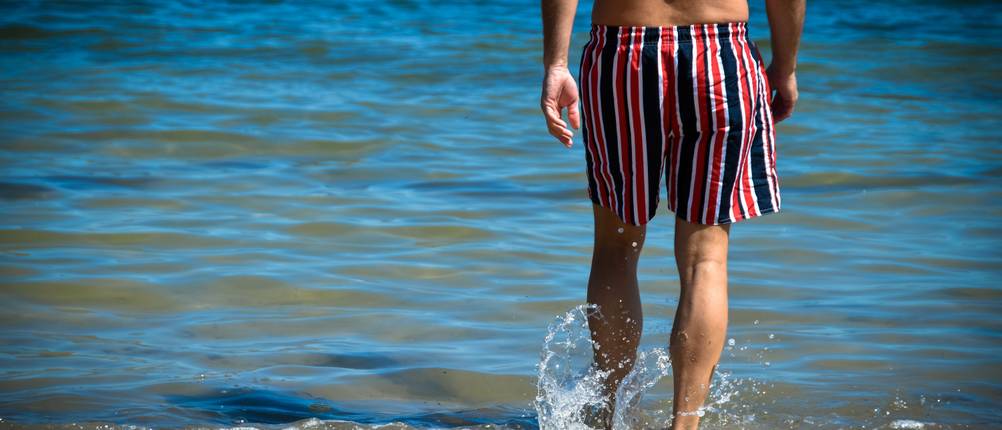 Badeshorts für Herren im Test: Mann geht zum Baden ins Meer.