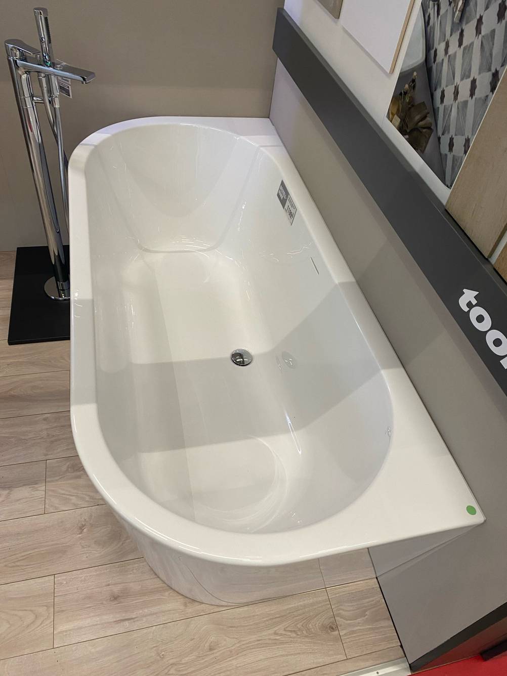 Ansicht auf eine weiße Duschbadewanne im Test, die über ein ovales Innendesign verfügt und mit einer geraden abschließenden Kante an einer Wand im Geschäft steht.