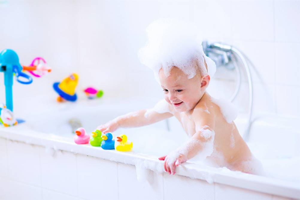 Badewannenspielzeug im Test: Ein Baby mit viel Schaum auf dem Kopf in der Wanne und viel Spielzeug.