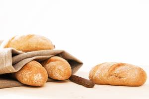 Bäckerleinen-Test: Kleine Baguettes in Bäckerleinen und ein Brotmesser liegen auf einer hellen Fläche auf. 