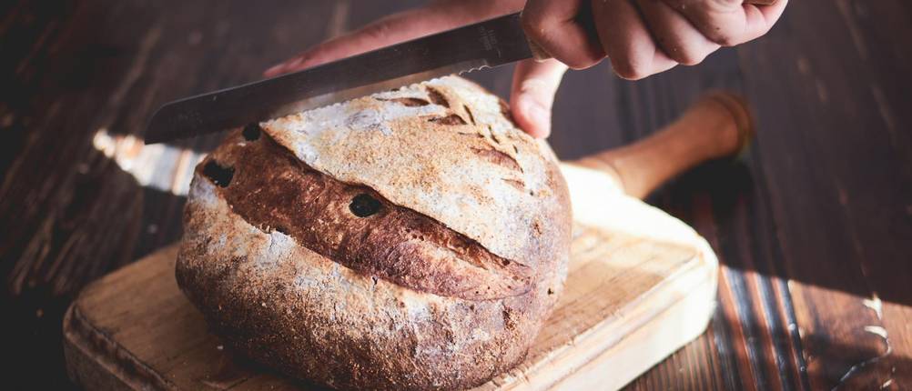 Bäckermesser-Test: Mann schneidet Brotlaib, das auf einem Holzbrett liegt, mit Messer