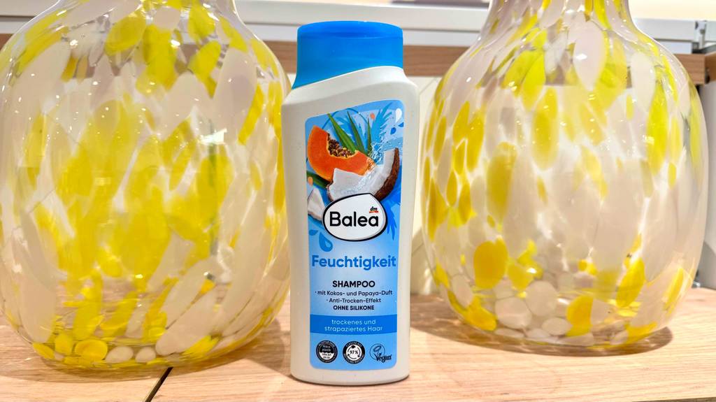 Eine Quetschflasche mit Feuchtigkeitsshampoo ohne Silikone im Test steht zwischen zwei Nachttischlampen.
