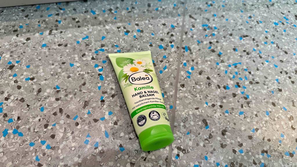Eine getestete Kamill-Handcreme in einer grünen Tube von Balea liegt auf einem Linoleumboden.