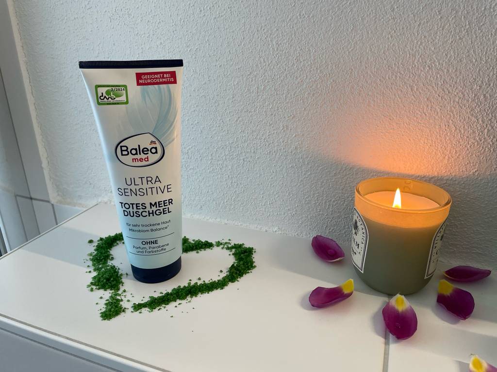 Eine Tube Duschgel für Neurodermitis steht zum testen in einem grünen Herz neben einer Kerze.