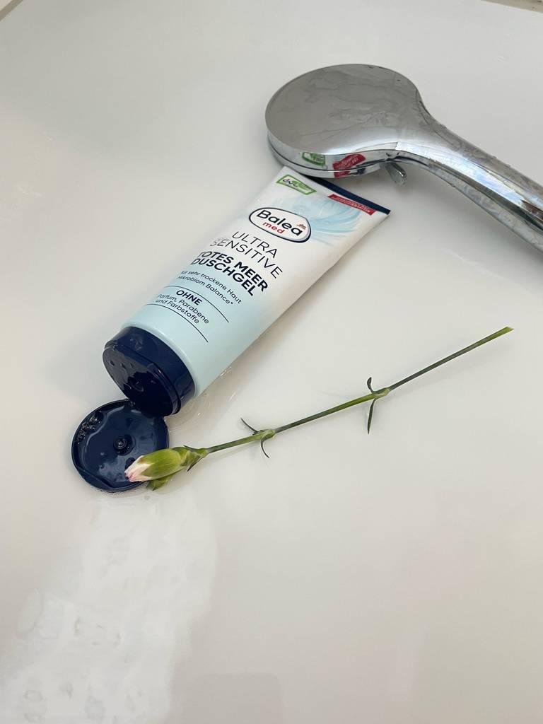 Eine geöffnete Tube Duschgel für Neurodermitis liegt zum testen vor einer Duschbrause.