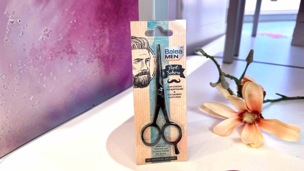 Im Test: Eine Bartschere steht mit Kartonblister vor einer Blume auf einem weißen Regal.