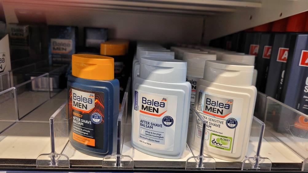 Eine hellblaue Kunststoffflasche Balea Men Aftershave im Test, 0 % Alkohol, steht mit weiteren Balea Men Produkten in einem DM Verkaufsregal.