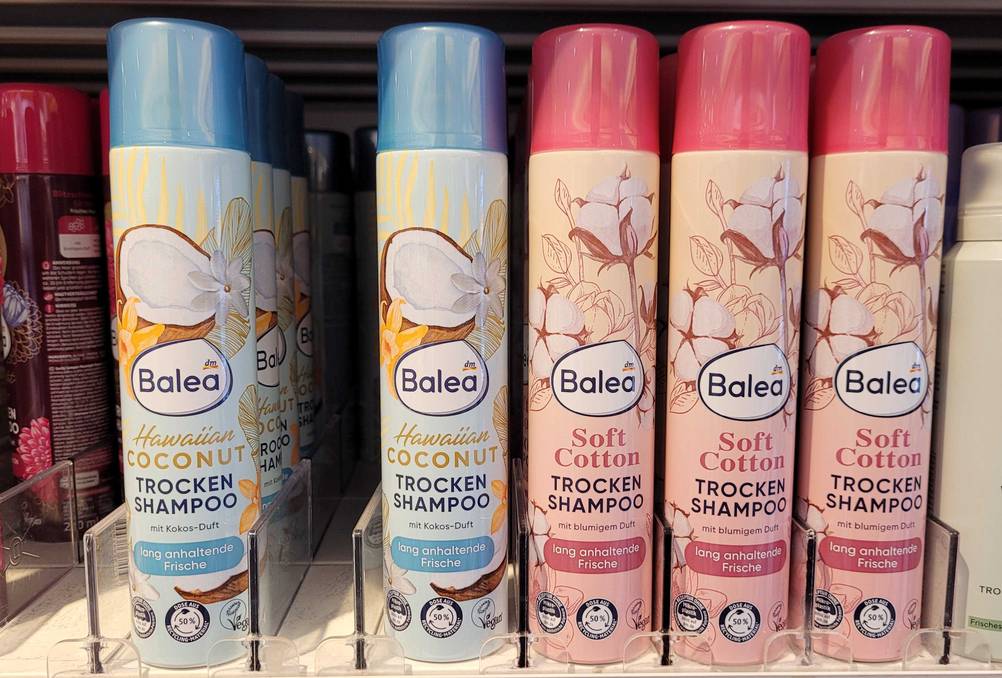 Im Test: Mehrere Dosen Trockenshampoo in verschieden Ausführungen stehen in einem Verkaufsregal nebeneinander.