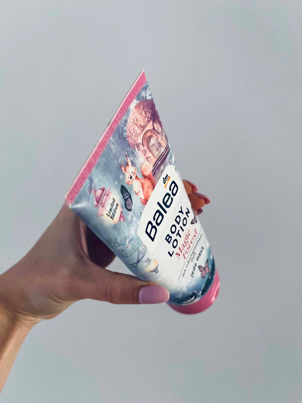Bodylotion-Test: Nahaufnahme der Oberseite einer Tube die eine Hand vor eine helle Wand hält.