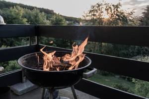 Flammen kommen aus einem Grill auf einem Balkon. Im Hintergrund sind Bäume zu sehen.