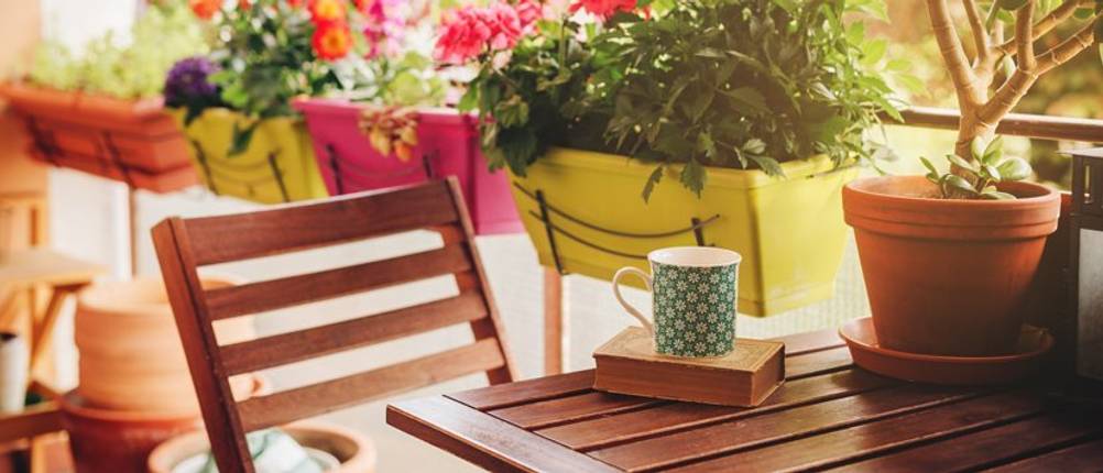 Balkonhängetisch-Test: Ein Holzbalkonhängetisch mit Stuhl auf einem Balkon mit bunten Blumenkästen.
