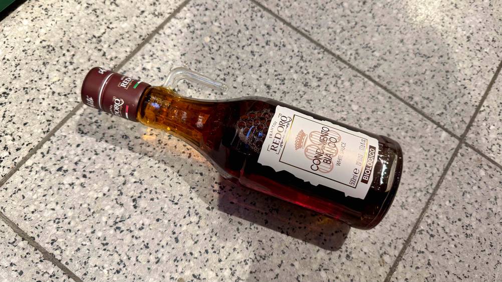 Eine Flasche des getesteten Balsamico bianco liegt horizontal auf eine Fließenboden.