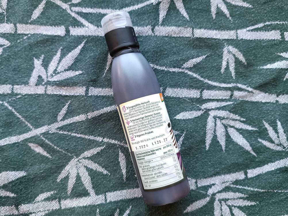 Rückseite einer Flasche Balsamico-Creme auf einer Stoffdecke.