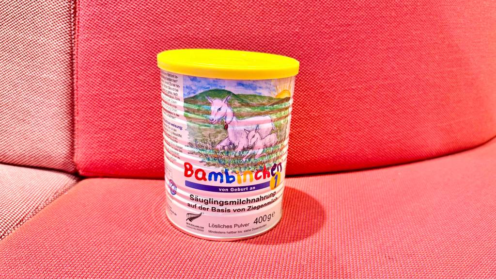 Eine Dose Ziegenmilch-Babynahrung steht zum testen auf einer roten Couch.