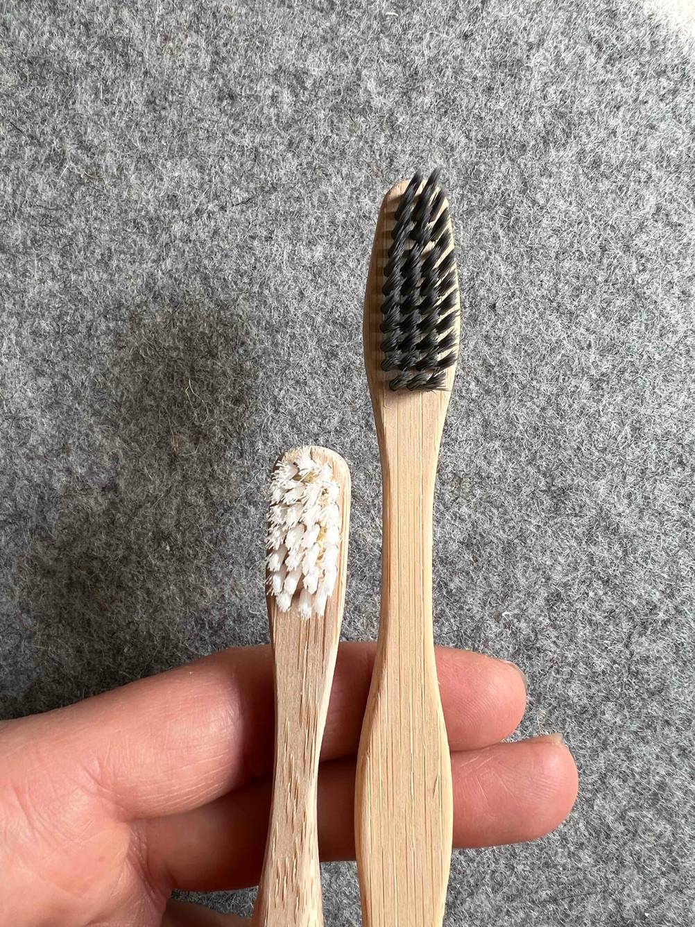 Nahaufnahme der Bürstenköpfe der getesteten Bambus-Zahnbürsten von einer Hand vor eine graue Fläche gehalten.