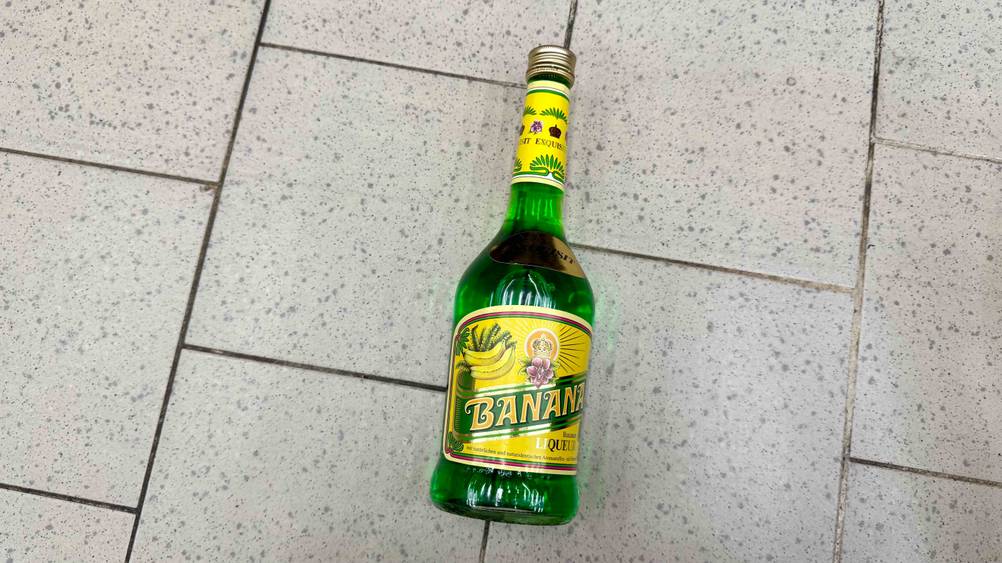 Eine Flasche des Bananenlikör im Test von oben auf einem Fließenboden liegend.