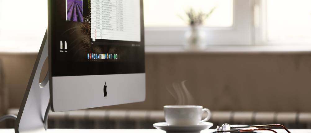 Banking-Software für den Mac im Vergleich: Ein iMac und eine Tasse Kaffee stehen auf einem Schreibtisch.