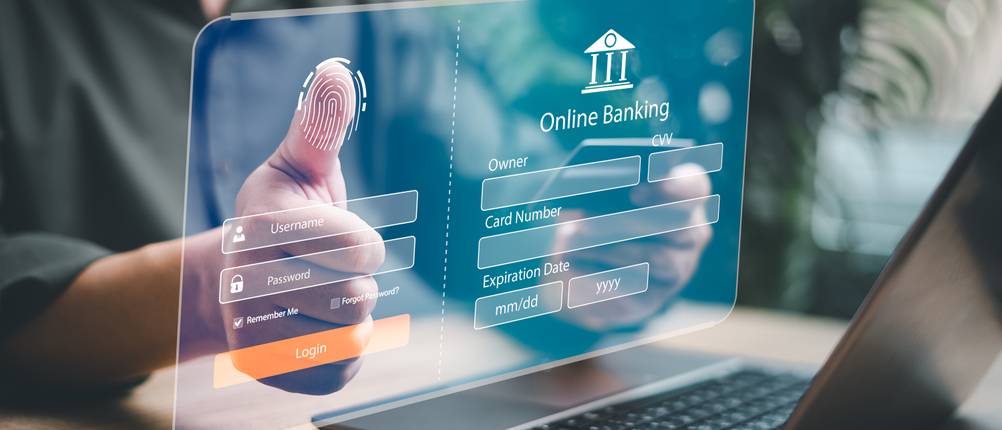 Banking-Software-Mac-Test: Ein Mann sitzt am Laptop und hält seinen Daumen an eine virtuelle Einblendung eines Anmelde-Fensters beim Online-Banking.