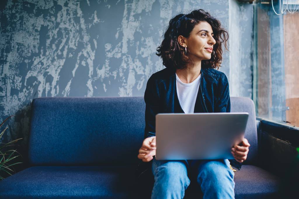 Banking-Software für den Mac im Vergleich: Eine Frau sitzt mit ihrem Macbook auf einer Couch und sieht aus dem Fenster.