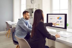 Banking-Software für den Mac im Test: Frau zeigt einem Kollegen Diagramme an einem Monitor.