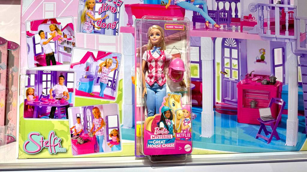 Eine verpackte Barbie-Puppe steht zum testen vor einem Puppenhauskarton.