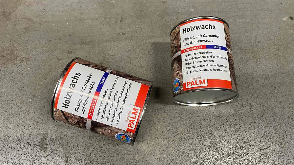 Holzwachs getestet: Zwei Dosen liegen schräg zueinander auf einem Steinboden.