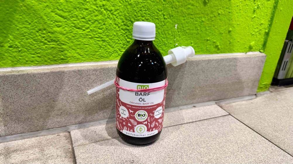 Vor einer grünen Wand steht das getestete Barf-Öl auf dem Boden.